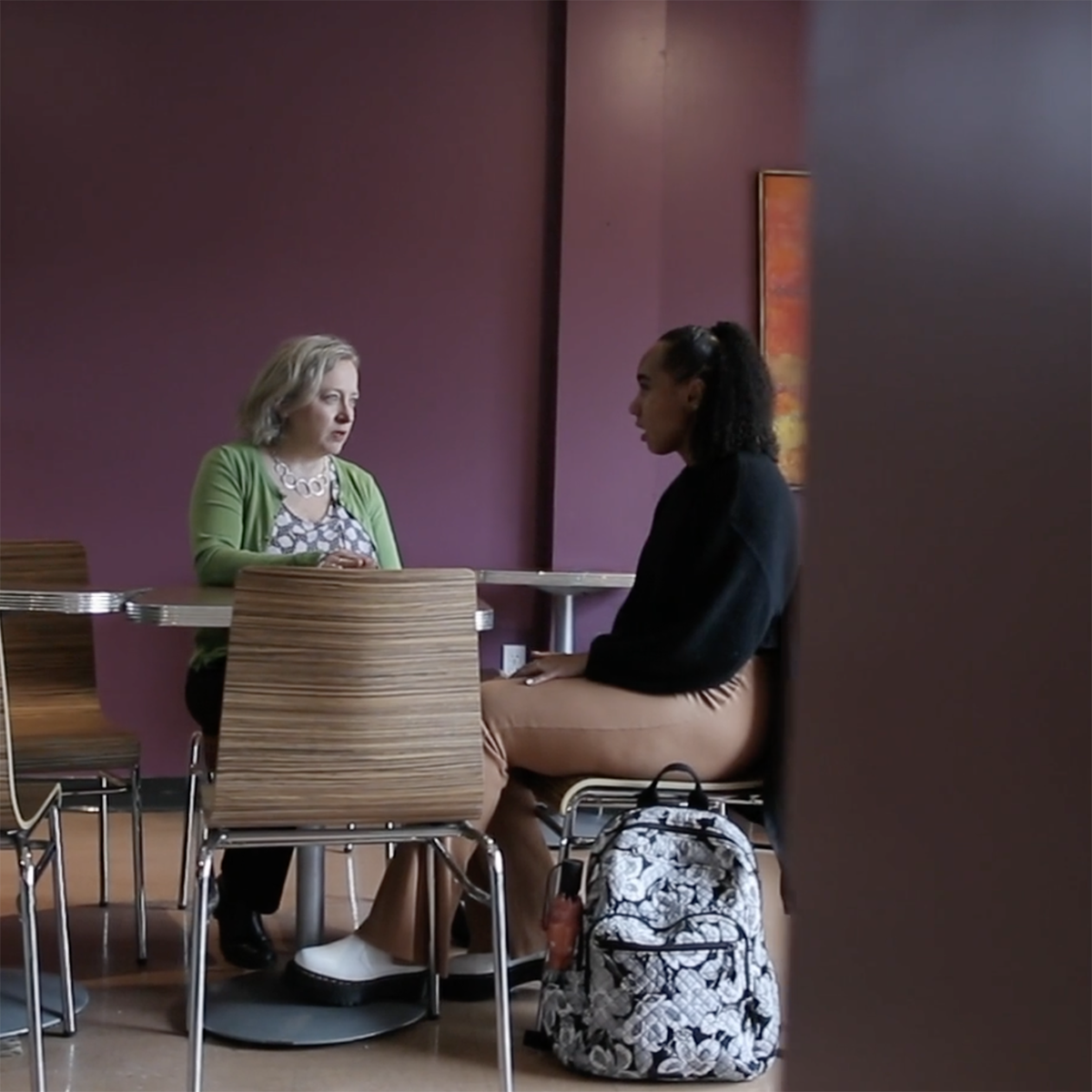 Photo of a faculty member and student seated at a table talking together